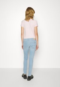 Světle růžové tričko s krátkým rukávem ve spojení se světle modrými skinny džíny. Tričko má jednoduchý design; džíny obsahují jemné detaily prošití a kapsy.
