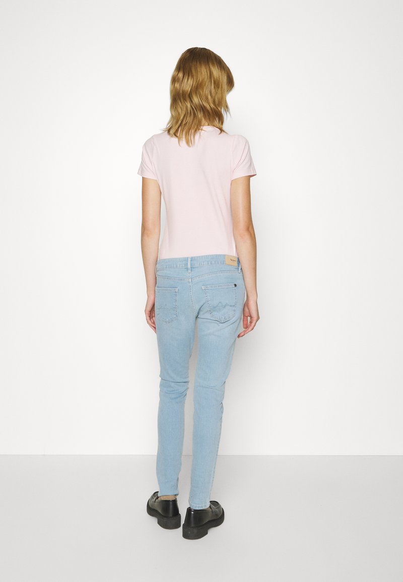 T-shirt rose clair à manches courtes associé à un jean skinny bleu clair. Le t-shirt présente un design simple ; le jean a des détails de couture subtils et des poches.