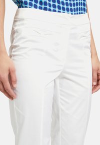 White tailored trousers made of smooth fabric, featuring two front pockets, a flat front design, and a slim fit.