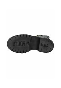 Suela de bota de goma negra con patrones de banda de rodadura profundos, logotipo "STEVE MADDEN" en relieve y un diseño de superficie texturizada.