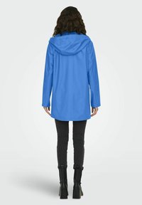 Blue waterproof jacket with a hood, reaching mid-thigh; paired with black skinny jeans and chunky black ankle boots. Smooth texture.