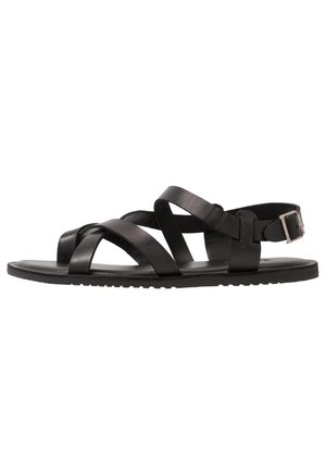 Black leather sandal with crisscross straps, flat sole, and adjustable ankle strap with silver buckle.