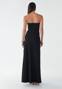 Melnā bezpiedurkņu maxi kleita ar pieguļošu augšdaļu, gludu tekstūru un rāvējslēdzēja aizdari aizmugurē. Apakšmala sasniedz grīdu.