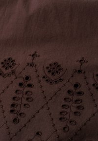 Brązowa tkanina z wyszywanymi kwiatowymi i liściastymi wzorami w symetrycznym układzie diamentowym, z teksturowanymi wypukłymi detalami ściegów.