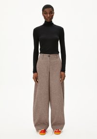 Schwarzer, langärmeliger Rollkragenpullover kombiniert mit hochgeschnittenen, weit geschnittenen, braun karierten Hosen und bunten Sneakers mit kontrastierenden Schnürsenkeln.