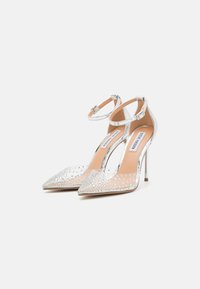 Tacones de aguja transparentes con acentos plateados, adornados con strass dispersos, con una correa en el tobillo y un diseño de punta afilada.