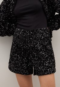 Black sequin shorts featuring a textured, shiny surface. The pattern consists of densely arranged sequins, creating a reflective look.