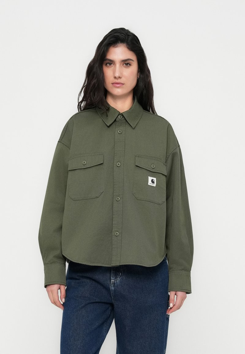 Πουκάμισο χακί πράσινο με κουμπιά, γιακά, δύο τσέπες στο στήθος και μπαλωμένο λογότυπο Carhartt. Κατασκευασμένο από υφασμάτινη υφή με άνετη εφαρμογή.