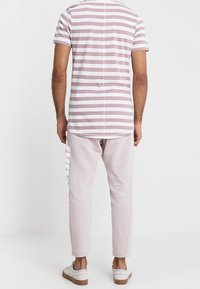 Camisa de manga corta a rayas en rosa claro y blanco, combinada con pantalones ajustados rosa pálido con acentos de raya blanca, usados con zapatos blancos.