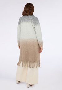 Cappotto lungo con colori a gradiente che vanno dal grigio al beige, realizzato in materiale morbido, con orlo frangiato e silhouette rilassata.