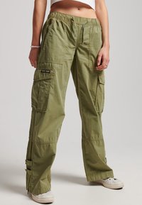 Groene cargobroek met een elastische taille, meerdere zijzakken en verstelbare enkelsluitingen. Gemaakt van lichtgewicht stof met een gladde textuur.