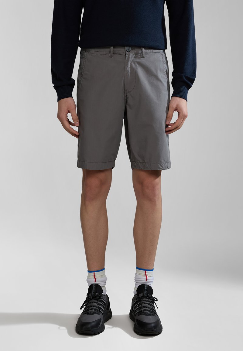 Grå shorts med flad front, subtile sømdetaljer og sidelommer, parret med sorte sportssko og hvide sokker med farvede accenter.