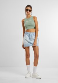 Top court côtelé vert clair avec du texte, associé à une jupe en denim bleu clair. Complété par des baskets blanches et des lunettes de soleil. Texture lisse.