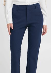 Marineblaue Hose mit glatter Textur, geradem Bein Design, dezenten Fronttaschen und einem sicheren Taillenband-Detail.