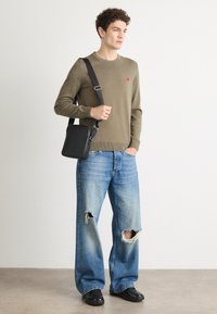 Khawlifarget strikkegenser, slitte blå jeans med store hull, svart crossover-veske og glansete svarte sko. Enkel og funksjonell design.