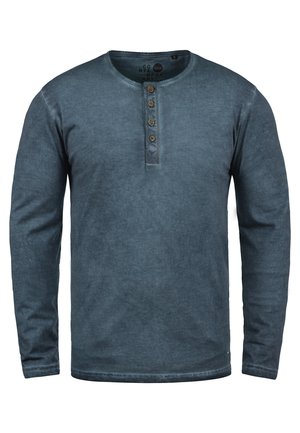 Chemise henley à manches longues d'une couleur bleu délavé, fabriquée en tissu doux. Dotée d'un col rond et de cinq boutons marron. Design uni.