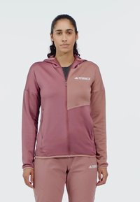 Värmande dragkedjsjacka i två nyanser av rosa, tillverkad av mjukt material. Har huva, framfickor och logodetalj på bröstet.