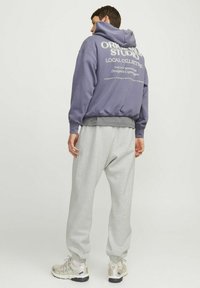 Purple hooded sweatshirt with white graphic text on the back, paired with light gray sweatpants and beige sneakers with black accents.