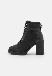 Botas de tobillo negras con tacón, acabado de charol liso, cuello de tela texturizada, cordones en la parte delantera y tacón robusto.