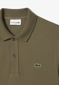 Olíva zöld Lacoste pólóing slim fit szabással, textúrált anyaggal, két gombos nyakkal és hímzett krokodil logóval a mellen.