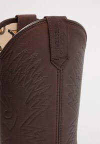 Botas de vaquero de cuero marrón con patrones en zig zag elevados, una costura bordada y una lengüeta con "KENTUCKY'S WESTERN" grabada.