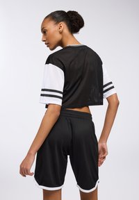 Top corto in rete nera con maniche e strisce bianche, abbinato a pantaloni shorts neri con bordi bianchi. Design in tessuto testurizzato e traspirante.