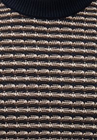 Gros plan sur un tissu de pull tricoté marron, beige et bleu foncé avec un col côtelé et un motif de point horizontal texturé.