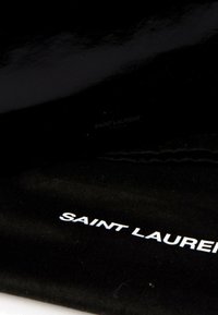 Tissu noir avec "Saint Laurent" imprimé en lettres blanches, montrant un gros plan du logo d'une marque de luxe sur un matériau doux.