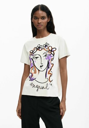 Moteris dėvinti baltą marškinėlį su spalvinga abstrakčia veido ir gėlių lankelio iliustracija bei juodas kelnes, stovinti prieš baltą foną.