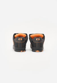 Black footwear with orange accents, padded collar, textured sole, and angular design features. Includes logos and stitching details.