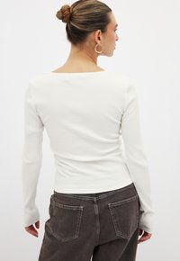 Top bianco a maniche lunghe con scollatura quadrata, dalla forma aderente e tessuto testurizzato, abbinato a jeans alto vita grigio scuro.