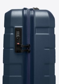 Valigia rigida blu navy con superficie testurizzata, doppia cerniera, lucchetto TSA integrato e forma rettangolare per durata e sicurezza.