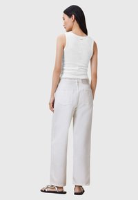 Top blanco de tirantes combinado con unos pantalones vaqueros anchos de tiro alto en blanco, que presentan una cintura deshilachada y pequeños detalles de bolsillo traseros. Sandalias negras completan el look.