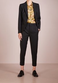 Černá upravená sako přes barevnou košili s květinovým vzorem, v kombinaci s černými zkrácenými kalhotami a černými koženými botami.