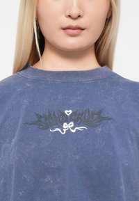 Modra grafična majica s sproščenim krojem. Ima črno-belo logo na prsih. Bombažna tkanina z obrabljenim videzom.