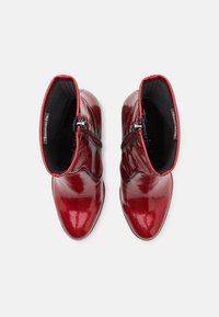 Bottines en cuir verni rouge avec une finition lisse et brillante, dotées d'une fermeture éclair sur le côté et d'un design à bout rond.