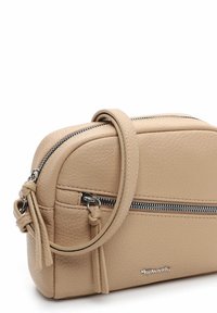 Beige leather crossbody bag with a textured finish, featuring silver zippers and a detachable strap. Rounded shape and minimalistic design.