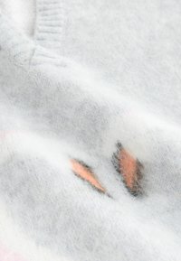 Tissu doux en laine blanche avec un motif brodé subtil représentant des formes floues orange et noires.