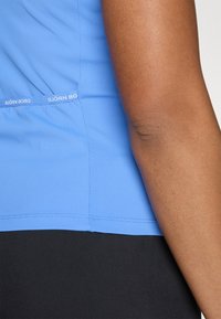 Blauwe sporttop met ribbeltextuur, een aansluitende pasvorm en zijbranding in het wit. De top is gecombineerd met zwarte onderkleding.