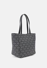 Borsa tote in bianco e nero con un motivo geometrico a pois, caratterizzata da manici lunghi neri e una forma rettangolare ampia.