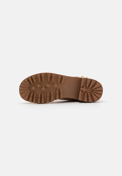 Semelle en caoutchouc marron avec des rainures profondes pour une traction optimale, présentant des motifs en relief et un bord lisse. Robuste et conçue pour la durabilité.