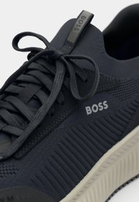 Dark blue sneaker with textured fabric upper, rounded toe, thick cream sole, and prominent "BOSS" logo on the side. Laces are gray.