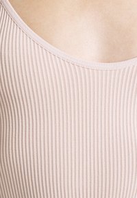 Světle růžový žebrovaný tílko s širokým výstřihem, vyrobené z jemné látky. Má vertikální pruhy a hladký povrch.