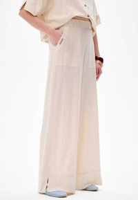 Hellebeige, weite Hose mit zwei Fronttaschen, hoher Taille und seitlichen Schlitzen am Saum, aus weichem, fließendem Stoff.