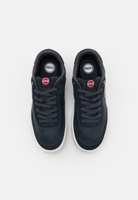 Baskets bleu marine en cuir lisse avec des accents texturés. Elles présentent des lacets ronds, un patch logo et une semelle en caoutchouc blanche avec des perforations.