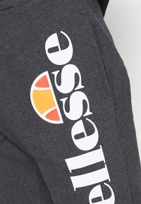 Pantalon de survêtement gris en mélange de coton. Caractérisé par un grand logo blanc sur le côté avec un accent coloré en orange et jaune. Comprend des poches.