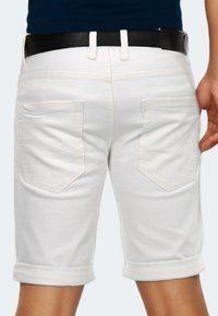 White denim shorts with rolled cuffs, featuring two back pockets with a chevron design. A black belt is worn at the waist.