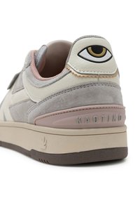 Sneaker mit einem grauen Wildleder- und beigen Lederobermaterial, das ein auffälliges Augendesign auf der Ferse und einen pinken Akzent auf der Sohle aufweist.