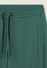 Pantaloni sportivi verdi con vita elasticizzata, cordini, tasca laterale e piccolo logo Freddy vicino alla tasca.