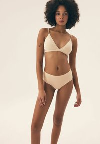 Beiges Bikini-Set mit einem dreieckigen Bralet mit dünnen Trägern und passenden hochgeschnittenen Hosen. Glatte, weiche Textur ohne Muster.